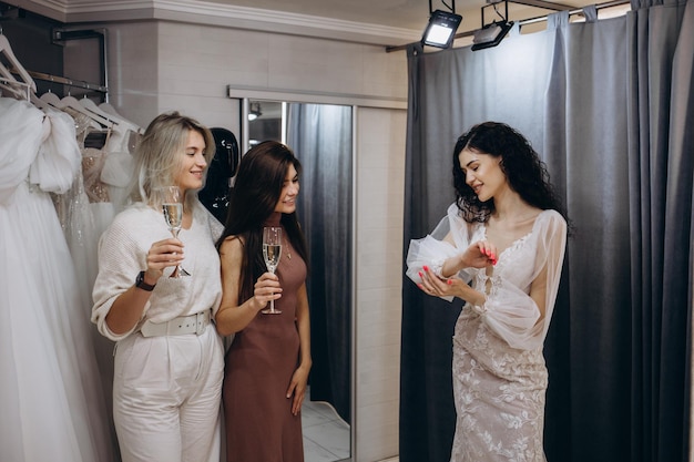 Beautiful bride is trying on an elegant wedding dress in modern wedding salon her friends are helping