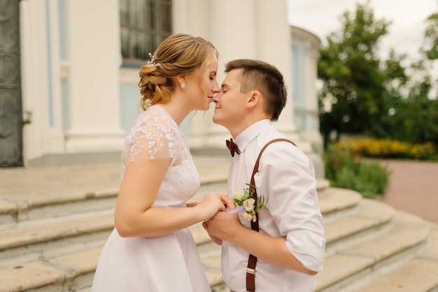 A beautiful bride kisses a stylish groom on the nose, a couple in love holds hands. Wedding day. Love, relationship concept.