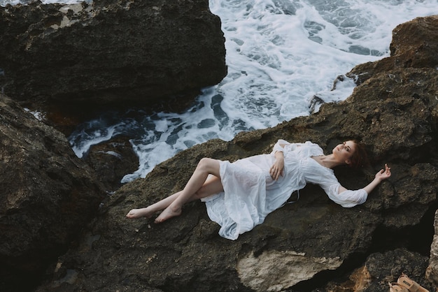 Beautiful bride Lies on his back on a stone cliff cloudy weather vacation concept