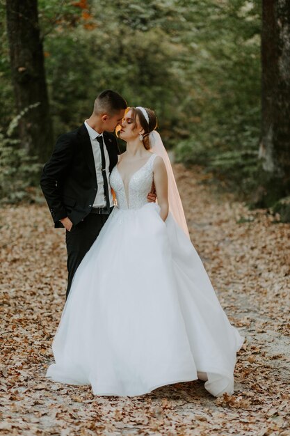 Beautiful bride in a long white dress. Handsome groom in a black suit. Couple in a summer park