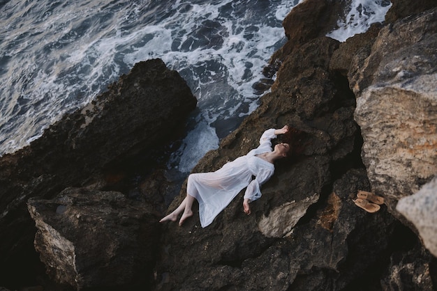 Beautiful bride in long white dress wet hair lying on a rocky cliff unaltered