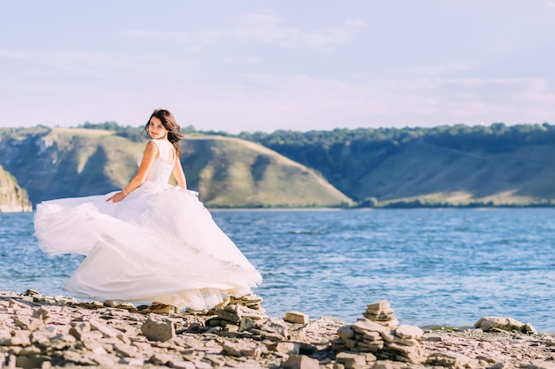 Beautiful bride in luxury white dress spinning around at lake