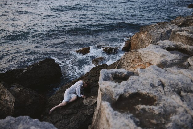 Beautiful bride lying on rocky coast with cracks on rocky\
surface view from above