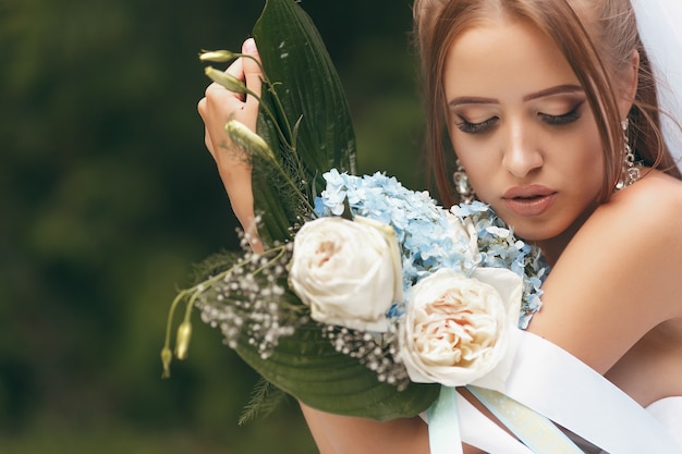 Beautiful bride in a magnificent wedding dress posing among greenery on the street. girl poses in a wedding dress for advertising. Bride concept for advertising dresses.