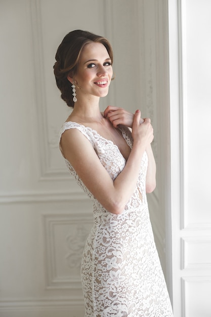 Beautiful bride posing in wedding dress in a white photo Studio. Mirror. Sofa. Bouquet. The door. Chandelier.