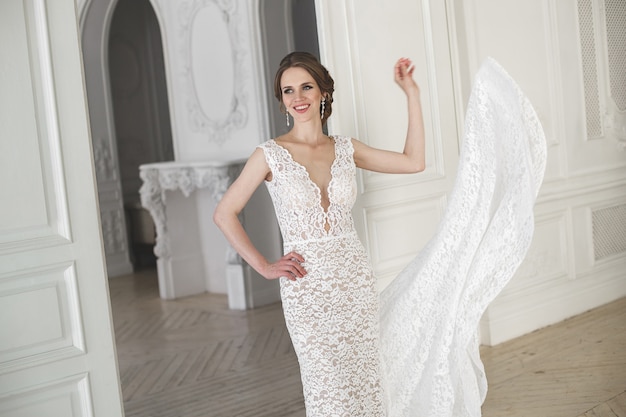 Beautiful bride posing in wedding dress in a white photo Studio. Mirror. Sofa. Bouquet. The door. Chandelier.