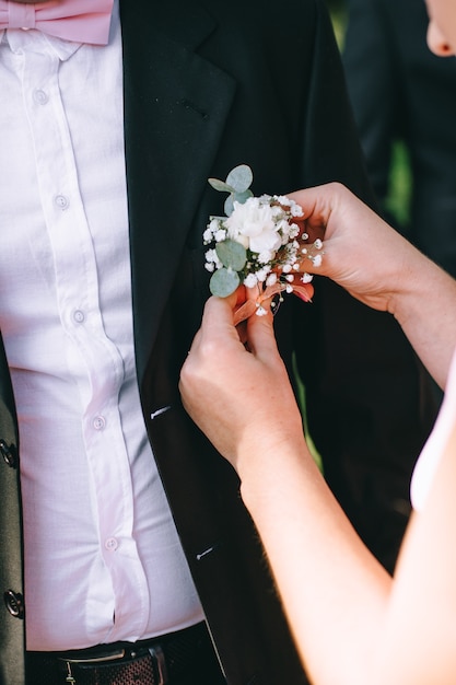 Beautiful bride putting on stylish simple boutonniere on groom black suit