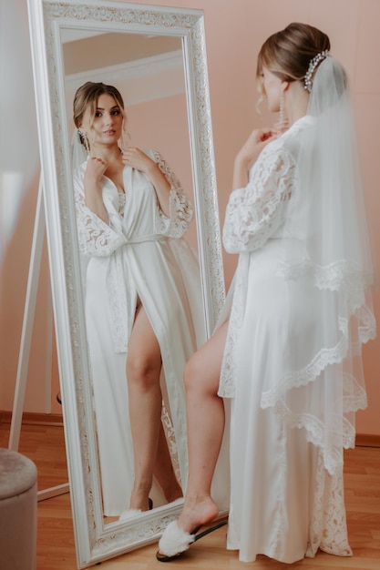 Beautiful bride in robe posing near window, wedding preparation