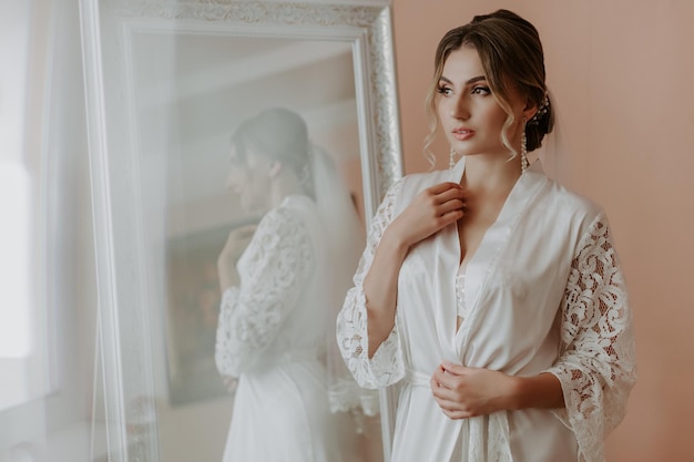 Beautiful bride in robe posing near window, wedding preparation