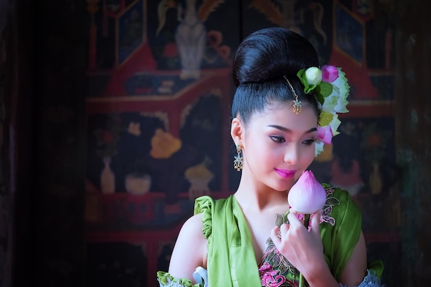 Photo beautiful bride in traditional clothing holding lotus water lily by wall