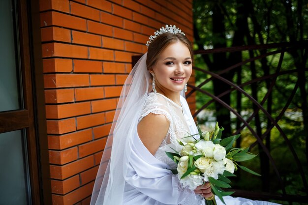 Bella sposa in velo e camice bianco si siede su una coperta con un bouquet da sposa nelle sue mani