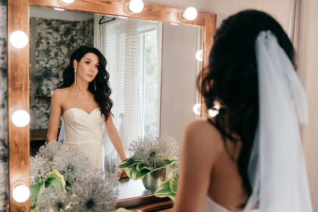 Красивая невеста в свадебном платье, глядя в зеркало