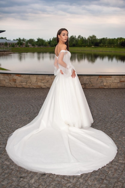 Beautiful bride in wedding dress posing on sunset near lake