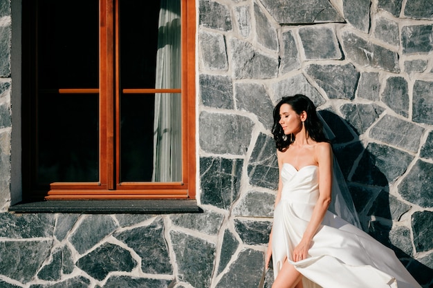 Beautiful bride in wedding dress posing over textured wall with window.