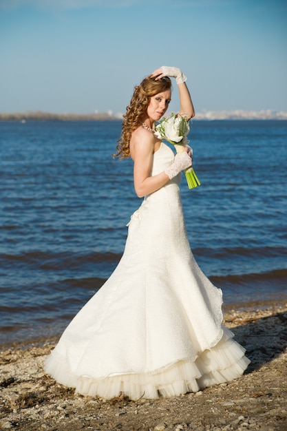 Beautiful bride in a white dress on coast of river in summer