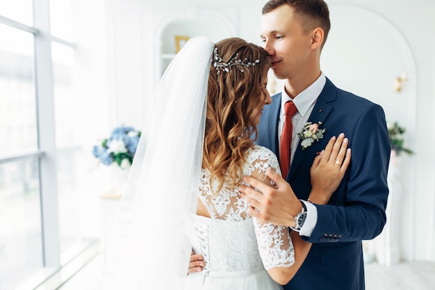 Beautiful bride in white dress and groom in suit, posing in white Studio interior, wedding