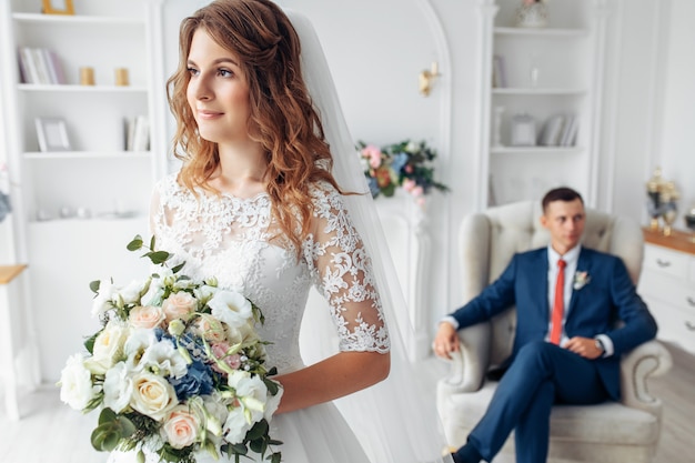 Красивая невеста в белом платье и жених в костюме, позирует в белом интерьере студии, свадьба
