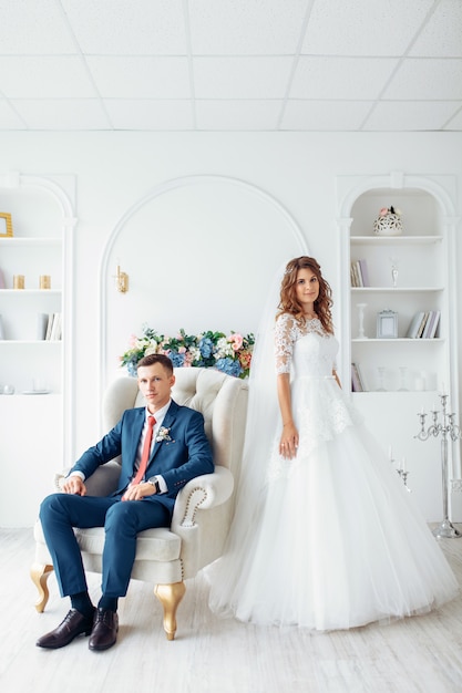 Beautiful bride in white dress and groom in suit, posing in white Studio interior, wedding