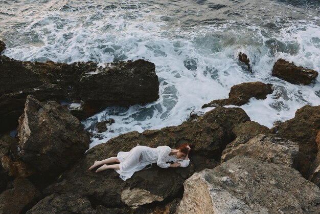 Beautiful bride in a white dress lying on a stone in a white dress vacation concept High quality photo