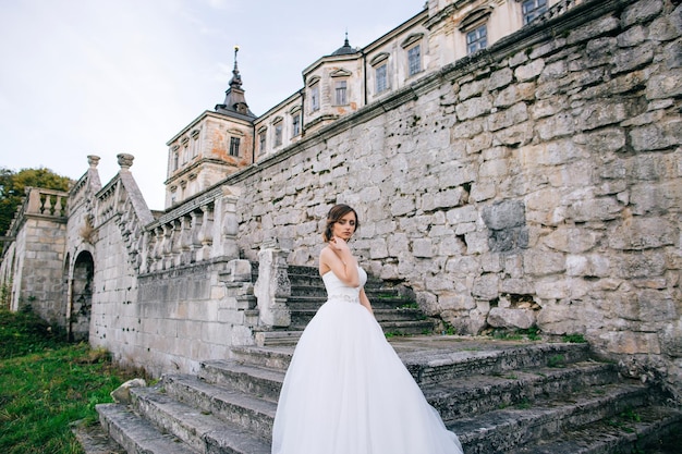 白いドレスを着た美しい花嫁が古い宮殿への階段を上がる