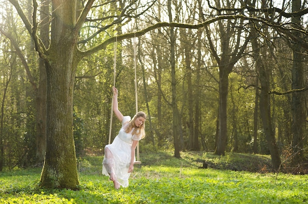 Beautiful bride in white wedding dress sitting on swing outdoors