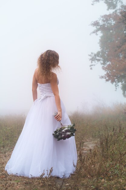 Beautiful bride with a bouquet on a background of a foggy field