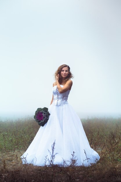 Bella sposa con un mazzo di fiori su un campo nebbioso