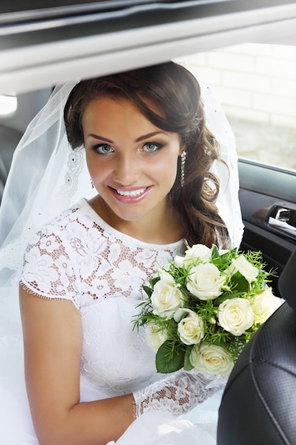 Beautiful bride with a bouquet of roses sitting in the car