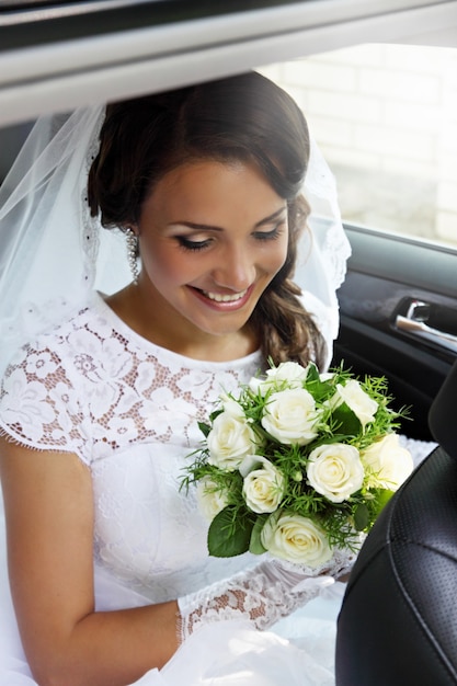 Beautiful bride with a bouquet of roses sitting in the car