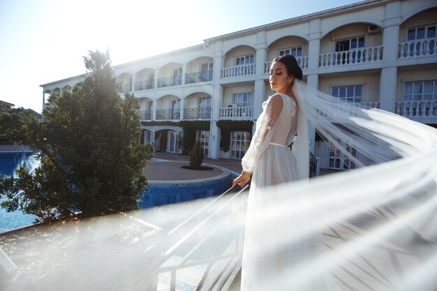 Beautiful bride with dark hair in luxurious wedding dress posing in balcony with sea view