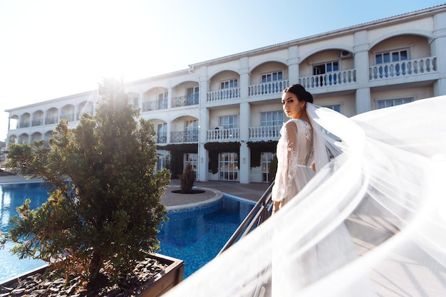 Beautiful bride with dark hair in luxurious wedding dress posing in balcony with sea view