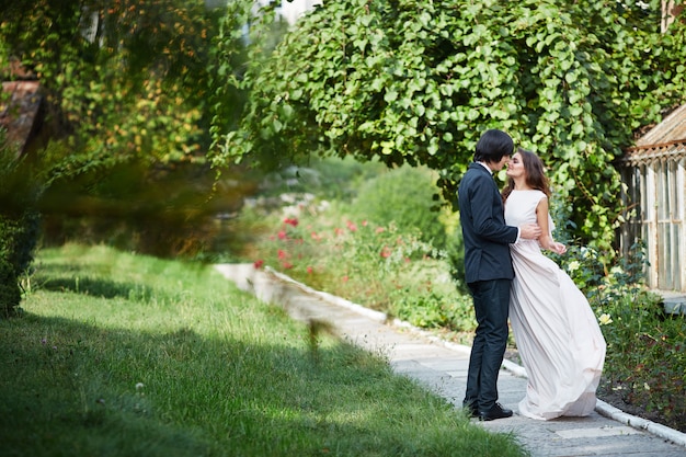 Bella sposa con lunghi capelli ricci e sposo in piedi vicino a vicenda a foglie verdi, foto del matrimonio, giorno del matrimonio, ritratto.