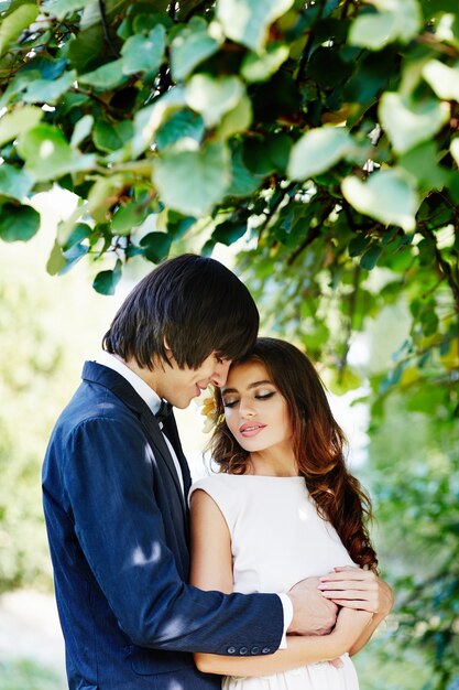 Bella sposa con i capelli lunghi e lo sposo in piedi vicino a vicenda a sfondo di foglie verdi, foto del matrimonio, bella coppia, primi piani.