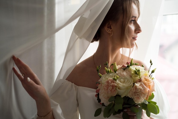 Beautiful bride with wedding bouquet near window