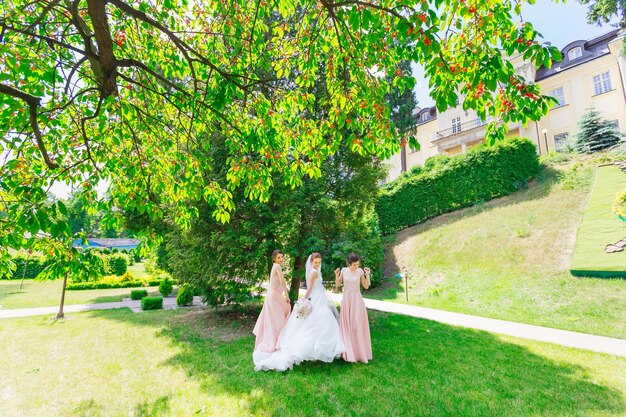 Красивые подружки невесты в персиковых платьях танцуют на зеленой траве У девушек хорошее настроение