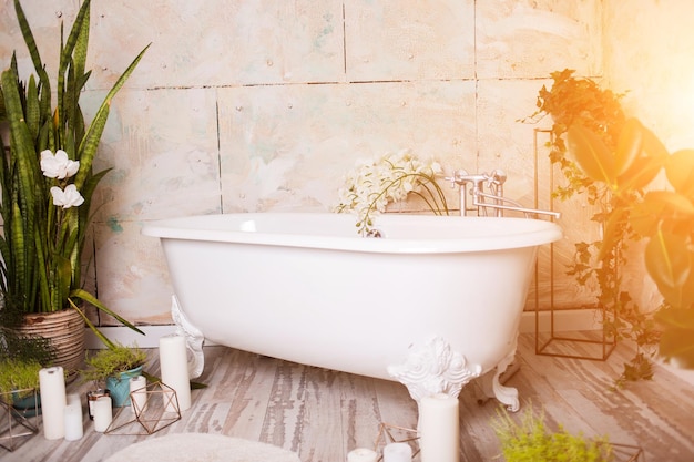 Beautiful bright bathroom with large white bath, green flowers, candles. House interior