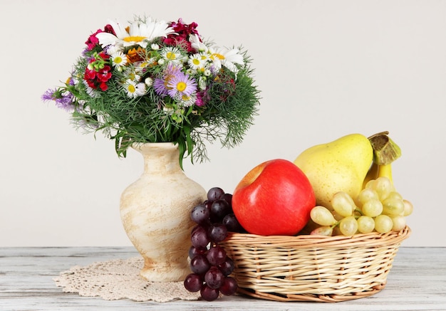 Beautiful bright flowers in vase with fruits on table on gray background