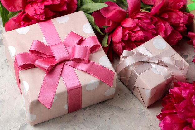 Beautiful bright pink flowers of peonies and a gift box on a bright concrete background.