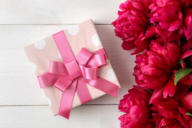 Beautiful bright pink flowers peonies and gift box on a white wooden background. top view.