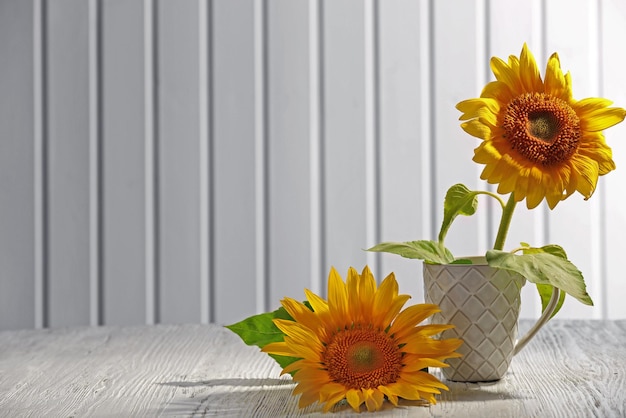 Beautiful bright sunflowers in cup on wooden background