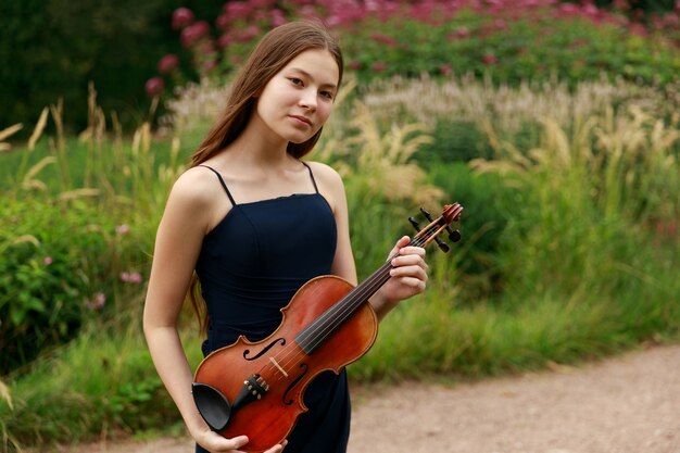 자연 속에서 바이올린을 든 아시아 외모의 아름다운 갈색 머리 소녀. 자연의 음악가. 고전 음악. 고품질 사진