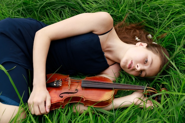 Beautiful brown-haired girl of Asian appearance with a violin in nature. musician in nature. classical music. High quality photo