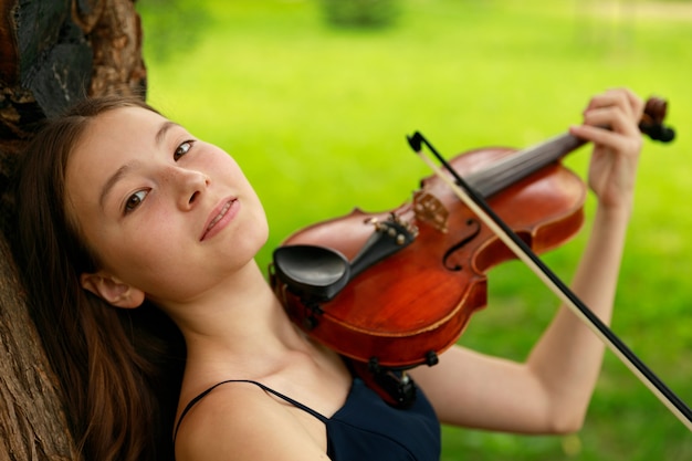 Beautiful brown-haired girl of Asian appearance with a violin in nature. musician in nature. classical music. High quality photo