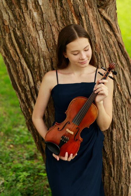 자연 속에서 바이올린을 든 아시아 외모의 아름다운 갈색 머리 소녀. 자연의 음악가. 고전 음악. 고품질 사진
