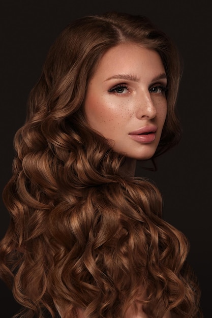 Bella ragazza dai capelli castani con capelli perfettamente arricciati e trucco classico bellezza viso e capelli