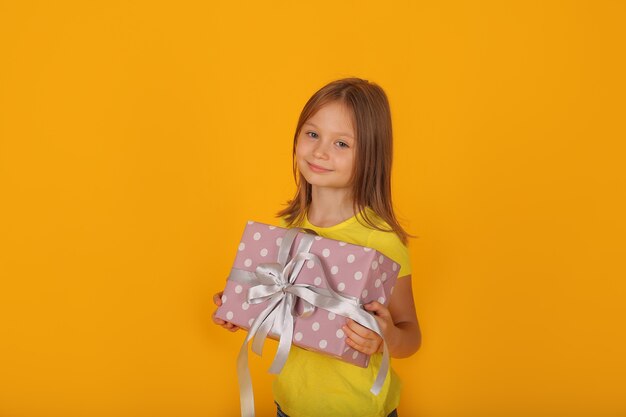 a beautiful brownhaired girl in a yellow Tshirt holds a gift box in her hands yellow background