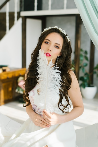 A beautiful brunette bride in a white wedding dress with a
tiara in her hair holds an ostrich feather in her hands.