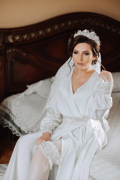 Photo a beautiful brunette bride with a tiara in her hair is getting ready for the wedding in a beautiful robe in boudoir style closeup wedding portrait photo