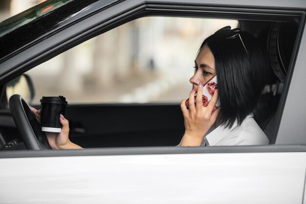 beautiful brunette driver sits in her car drinking coffee and talking on the phone