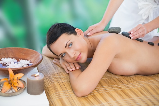 Beautiful brunette enjoying a hot stone massage smiling at camera